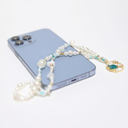 A phone hanger with white and blue beads, and an ocean-themed charm, displayed on a blue smartphone.